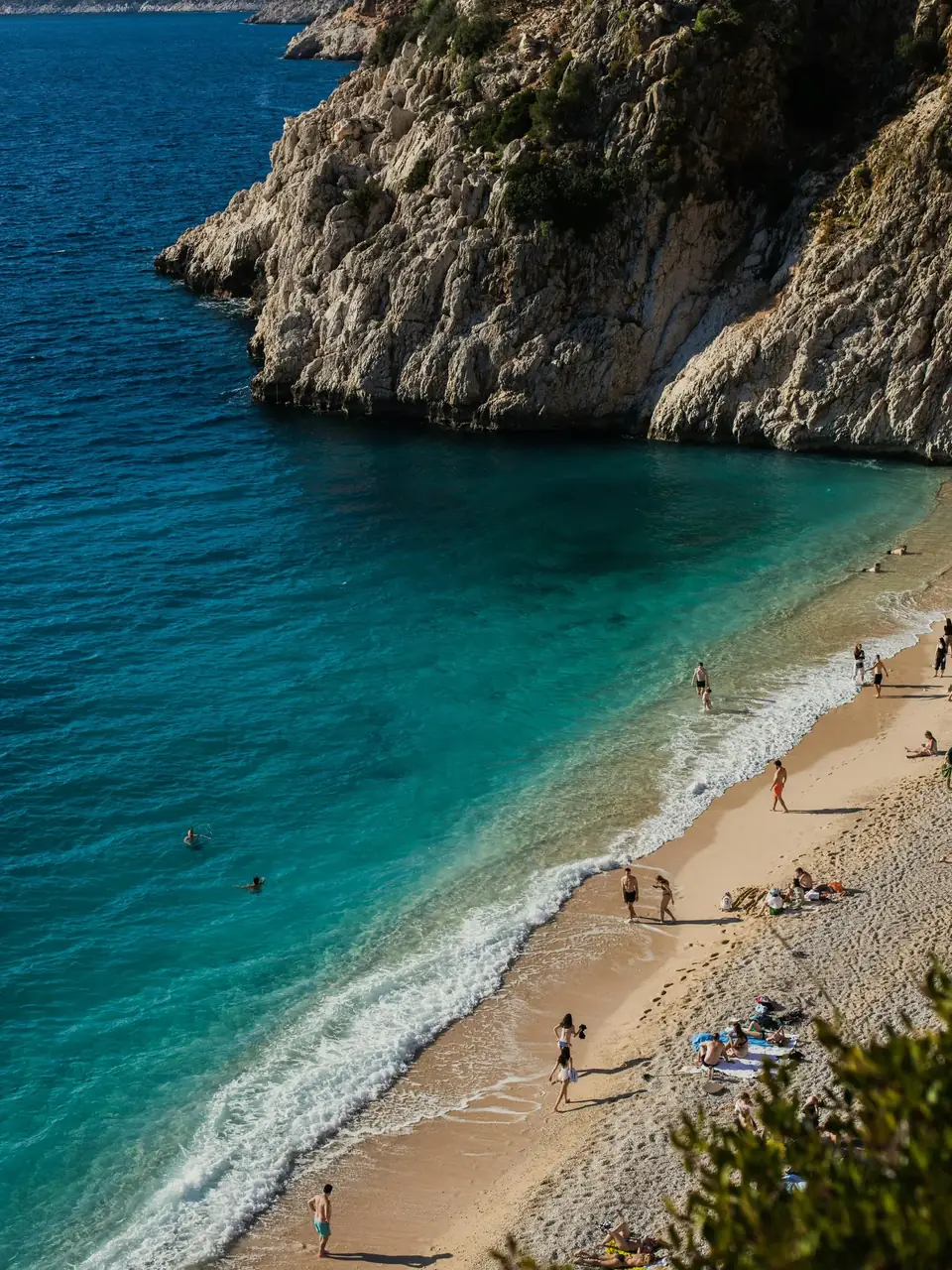 Turquoise water, a pale beach with bathers and a limestone cliff above it